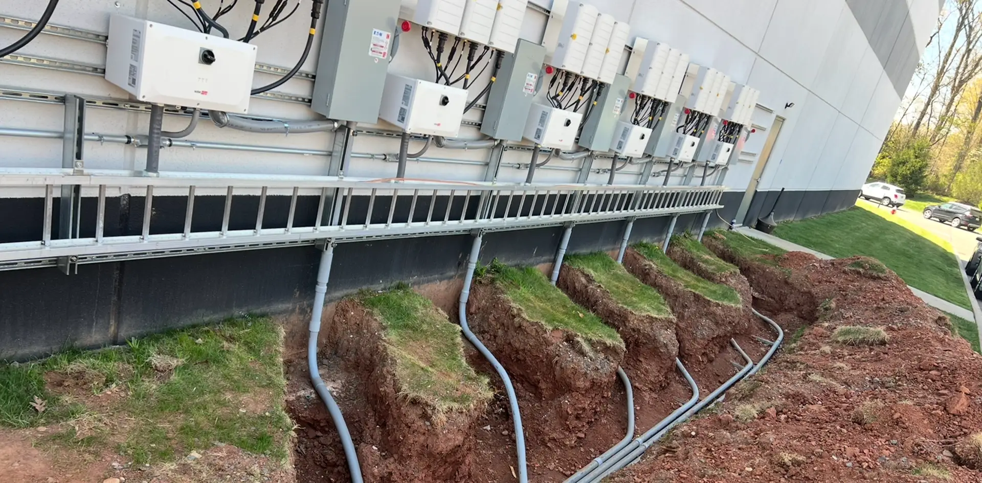 Installation of commercial electrical boxes with wires being run in a dugout trench in the ground.